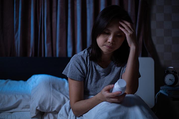 Woman sitting up in bed reading a pill bottle