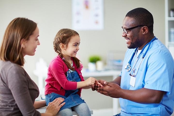 A young child and her mom talking with a doctor in the clinic. 